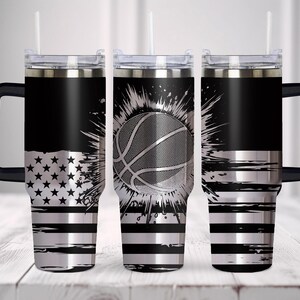 May include: Three black and silver insulated tumblers with handles and straws. One features a silver American flag design, another a basketball graphic, and the third has silver stripes. The tumblers are designed for cold beverages.