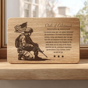 Könnte beinhalten: Eine rechteckige Holzplatte mit einer lasergravierten Abbildung eines knienden Soldaten mit Gewehr und einer amerikanischen Flagge. Der Text lautet Oath of Enlistment, gefolgt vom vollständigen Eid und drei Sternen in der unteren rechten Ecke.