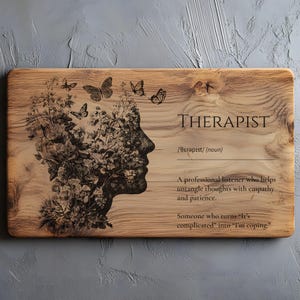 Puede incluir: Placa de madera rectangular con la palabra "THERAPIST" y una definición. El diseño presenta una silueta de rostro llena de flores y mariposas. La placa incluye el texto: "Un oyente profesional que ayuda a desenredar los pensamientos con empatía y paciencia."