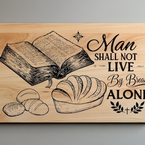 May include: A wooden chopping board with a black and white illustration of a bible, bread, and the text "Man shall not live by bread alone".