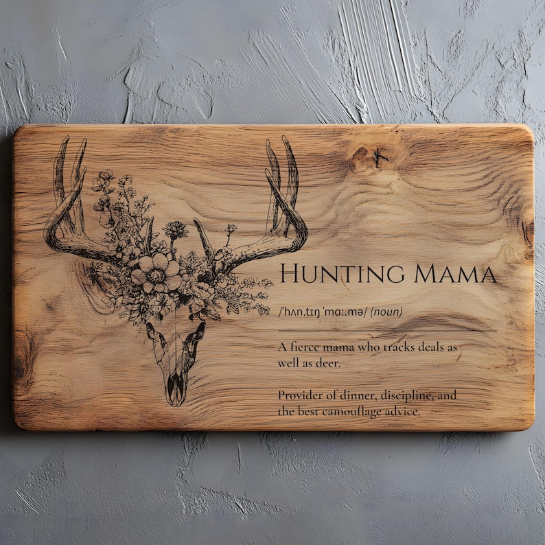 K&ouml;nnte beinhalten: Rechteckiges Holzschneidebrett mit dem Text "HUNTING MAMA" und einem Hirschsch&auml;del-Design mit floralen Akzenten. Der Text enth&auml;lt eine Definition und eine Beschreibung einer "wilden Mama".