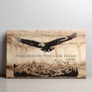 May include: Wooden wall art featuring a black eagle in flight above a mountain range. The text "SOAR HIGH ON WINGS LIKE EAGLES" and "Isaiah 40:31" are printed below the eagle. The artwork has a natural wood grain background.