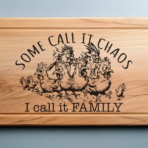 以下が含まれることがあります： 鶏の白黒のイラストと「Some call it chaos I call it family」というテキストが書かれた木製のまな板です。