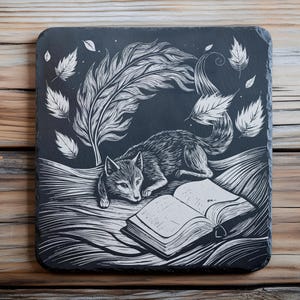 Puede incluir: Posavasos cuadrado de pizarra negra con una ilustración blanca de un zorro leyendo un libro. También se representa una gran pluma y hojas. El posavasos está sobre una superficie de madera. Aproximadamente 10 cm.