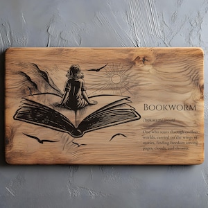 Peut inclure: Planche à découper en bois avec une gravure détaillée. Le motif représente une personne assise sur un livre ouvert, avec le mot "BOOKWORM" et sa définition. L'œuvre comprend un soleil, des oiseaux et des lignes fluides.