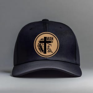 May include: Black baseball cap with a circular patch featuring a lion's head, a cross, and the words "MAN of Faith" in a serif font. The cap has a curved brim and a button on top. The background is a solid gray.