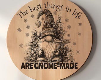 May include: A circular light-colored wooden plaque featuring a black engraved illustration of a gnome wearing a patterned hat, surrounded by snowflakes and foliage. The text reads, The best things in life ARE GNOME-MADE in black lettering.