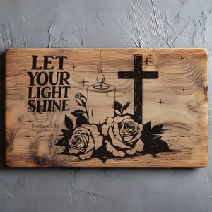 May include: Wooden plaque with engraved design. Features the text "LET YOUR LIGHT SHINE" and "Matthew 5:16". Includes a candle, cross, and roses. The design is in black against the natural wood grain.