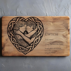 May include: Wooden cutting board with a heart-shaped design featuring two embracing figures. The word "CWTCH" and its definition are etched into the wood. The board is made of light brown wood.