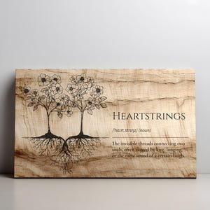 May include: Wooden wall art featuring two stylized trees with interconnected roots and floral crowns. The text "HEARTSTRINGS" is displayed, along with a definition. The artwork is on a light brown, textured wooden surface.