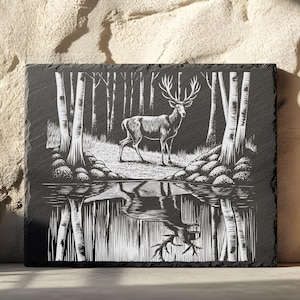 Puede incluir: Una placa de pizarra negra con una imagen grabada en blanco de un ciervo de pie en un bosque con un reflejo en un lago debajo. El ciervo tiene cuernos y mira hacia la derecha.