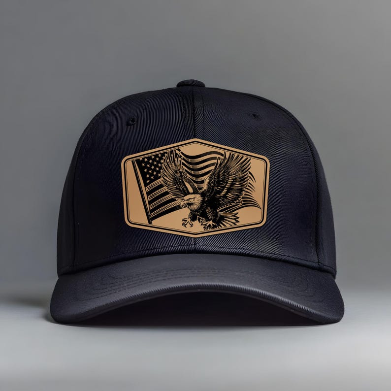 May include: A black baseball cap featuring a tan leather patch with an American flag and a detailed eagle illustration. The cap has a curved brim and a structured crown, suitable for outdoor wear.
