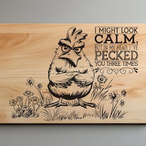 May include: Wooden cutting board with a humorous design. A stern-looking chicken illustration is etched on the light-colored wood, along with the text "I MIGHT LOOK CALM, BUT IN MY HEAD, I'VE PECKED YOU THREE TIMES."
