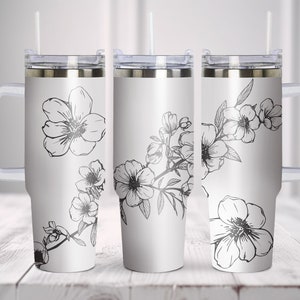 Puede incluir: Vaso aislado blanco con tapa, asa y pajita plateadas. El vaso presenta un diseño floral negro. El diseño floral incluye flores y hojas. El vaso está diseñado para contener aproximadamente 887 ml.