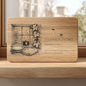 May include: A rectangular wooden board featuring a laser-engraved illustration of a window with autumn leaves, a pie, and a pot. The text reads: THANKSGIVING, /θæŋksɡɪvɪŋ/ noun, A feast of thanks, a table of stories, a day when love smells like pie.