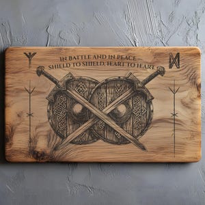 Puede incluir: Placa de madera con temática vikinga. Presenta dos espadas cruzadas sobre dos escudos, con el texto "IN BATTLE AND IN PEACE SHIELD TO SHIELD, HEART TO HEART". El diseño está grabado en negro sobre una superficie de madera marrón claro.