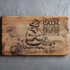 May include: A rectangular wooden cutting board with a humorous engraved design. The design features an angry chicken with crossed arms, surrounded by flowers and grass. Text reads, "I MIGHT LOOK CALM, BUT IN MY HEAD, I'VE PECKED YOU THREE TIMES."