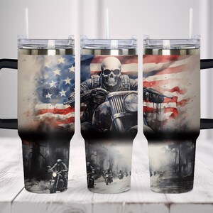 May include: A stainless steel tumbler with a black handle and lid, featuring a watercolor design of a skull riding a motorcycle in front of an American flag. The design includes a biker gang on a road.