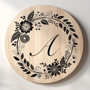 May include: A round wooden sign with a floral wreath design in black. The letter "A" is in the center of the sign. The wreath features various flowers and leaves. The wood has a light, natural finish.