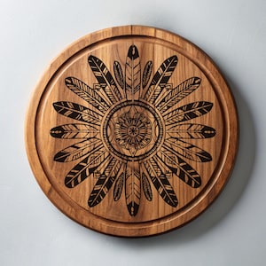 Puede incluir: Una tabla de cortar redonda de madera con un diseño en blanco y negro de plumas y un mandala en el centro.