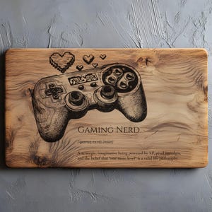 Puede incluir: Tabla de cortar de madera con un grabado detallado de un mando de videojuegos y corazones pixelados. El texto "GAMING NERD" está debajo, junto con una definición y una cita sobre juegos.