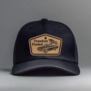Puede incluir: Gorra de béisbol negra con visera curva. La gorra presenta un parche de cuero color canela con las palabras "Freedom Fueled" y una ilustración de una camioneta vintage con una bandera estadounidense.