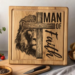 May include: Wooden cutting board with a carved lion's face and a cross. The words "MAN OF Faith" are printed on the board. The board is light brown with a dark brown design. The board has a square shape with a recessed edge.