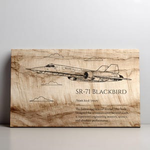 May include: A rectangular wooden plaque featuring a black line drawing of an SR-71 Blackbird aircraft. Below the aircraft, the text reads SR-71 BLACKBIRD, /blæk.bɜːd/ (noun), and a description of the aircraft as the fastest operational jet.