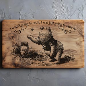 Könnte beinhalten: Holzschneidebrett mit einem Winnie-the-Pooh-Design. Das Bild zeigt Pooh, der nach einem Honigglas greift, mit dem Text "I wasn't going to eat it, I was just going to taste it." Das Brett hat eine natürliche Holzmaserung.