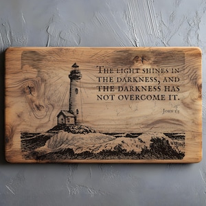 May include: Wooden plaque featuring a lighthouse engraving. The design shows a lighthouse on a rocky shore with waves, and the text "THE LIGHT SHINES IN THE DARKNESS, AND THE DARKNESS HAS NOT OVERCOME IT. JOHN 1:5". The plaque has a natural wood grain.