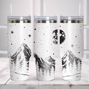 May include: Three stainless steel tumblers with a white background and a black mountain range design. The tumblers have a clear lid and a clear handle. The design also includes a moon and stars.