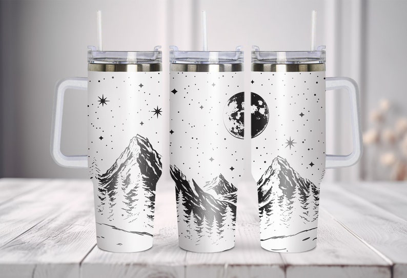 May include: Three stainless steel tumblers with a white background and a black mountain range design. The tumblers have a clear lid and a clear handle. The design also includes a moon and stars.