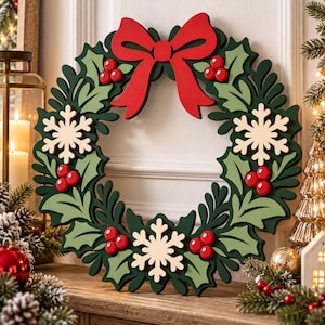 May include: A circular holiday wreath featuring layered dark and light green holly leaves, bright red berries, three cream-colored snowflakes, and a large red bow at the top. The design is constructed from flat, cutout shapes.