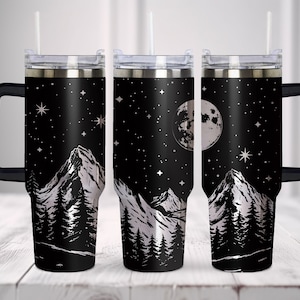 May include: Three stainless steel travel mugs with black handles and lids. The mugs feature a black and white design of mountains, a full moon, and stars against a black background.