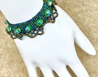 May include: A green and brown beaded bracelet with a scalloped edge and clear green crystal accents.