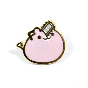 May include: A pink enamel pin with a gold border. The pin features a cartoon character with a chainsaw on its head. The character has a white mustache and a small white mouth. The pin is on a white background.