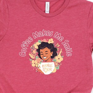 以下が含まれることがあります： 「Coffee Makes Me Smile」の文字が円形にデザインされた赤いTシャツ。デザインは、花に囲まれコーヒーカップを持った、笑顔の人物が特徴です。カップには「MAIMEEE COFFEE」の文字が書かれています。