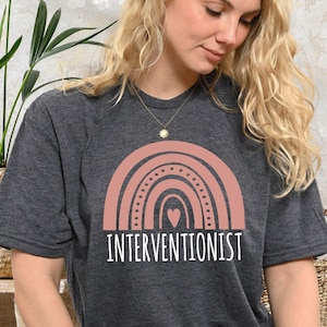 May include: A dark grey t-shirt with a pink rainbow graphic and the text "Interventionist" in white.