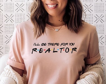 May include: A woman wearing a pink t-shirt with the text "I'll be there for you - REALTOR" in a colorful font. She is sitting in a white chair with a white blanket draped over her legs. A cactus plant is in a white pot on a wooden table next to the chair.