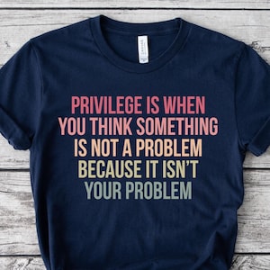 May include: Navy blue t-shirt with the text "PRIVILEGE IS WHEN YOU THINK SOMETHING IS NOT A PROBLEM BECAUSE IT ISN'T YOUR PROBLEM" in pink, orange, yellow, and green. The shirt is knotted at the bottom.