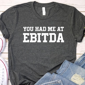 May include: A dark gray t-shirt with the text "You had me at EBITDA" printed in white.
