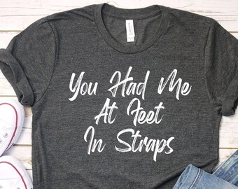 May include: A dark gray t-shirt with the text "You Had Me At Feet In Straps" printed in white.