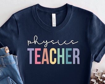 May include: A navy blue t-shirt with the text "physics TEACHER" in rainbow colors. The shirt is folded and displayed with a pair of blue jeans and a bouquet of white flowers.