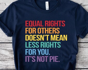 May include: A navy blue t-shirt with the text "EQUAL RIGHTS FOR OTHERS DOESN'T MEAN LESS RIGHTS FOR YOU. IT'S NOT PIE." in a rainbow of colors. The shirt is displayed on a light wood grain surface.