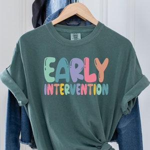 May include: A green t-shirt with the text "EARLY INTERVENTION" in colorful, balloon-like letters.