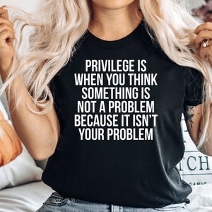 May include: A black t-shirt with white text that reads "Privilege is when you think something is not a problem because it isn't your problem."