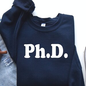 May include: A navy blue sweatshirt with white text that reads "Ph.D."