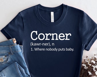May include: A navy blue t-shirt with white text that reads "Corner (kawr-ner), n 1. Where nobody puts baby."