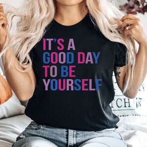 May include: A black t-shirt with the text "It's a good day to be yourself" in pink, blue, and purple lettering.