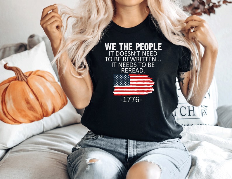 K&ouml;nnte beinhalten: Schwarzes T-Shirt mit einem abgenutzten amerikanischen Flaggen-Motiv und dem Text "WE THE PEOPLE IT DOESN'T NEED TO BE REWRITTEN... IT NEEDS TO BE REREAD. -1776-"